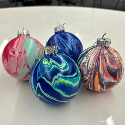 Image depicts four Christmas tree ornaments coated in acrylic pour paints.